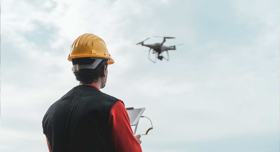 Inspector in hard hat flying drone over shingle roof